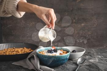 Woman preparing tasty granola with yogurt on grey background�