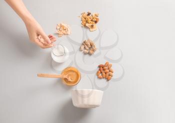 Female hand with jug of yogurt, tasty granola and ingredients on white background�