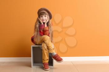 Cute little girl in autumn clothes sitting near color wall�