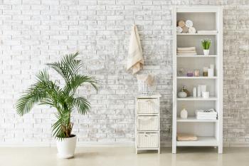 Shelf unit with towels and cosmetics near brick wall in bathroom�