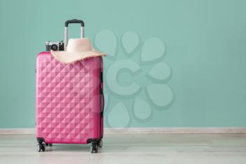 Suitcase, photo camera and hat near color wall. Travel concept�