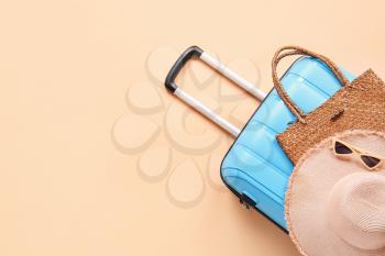 Suitcase with hat, bag and sunglasses on color background�