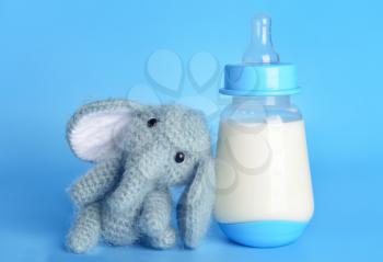 Bottle of milk for baby and toy on color background�