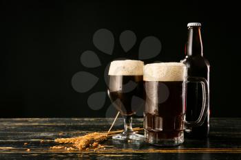 Glassware with fresh beer on table against dark background�