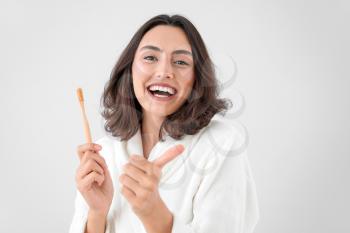 Beautiful young woman with toothbrush showing thumb-up gesture on light background�