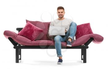 Young man with laptop sitting on sofa against white background�