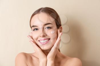 Beautiful young woman applying cream on her face against color background�