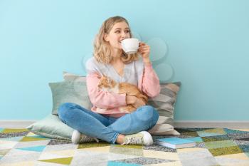 Beautiful young woman with cute cat drinking tea at home�