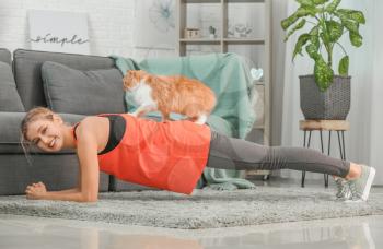 Young woman with cute cat practicing yoga at home�