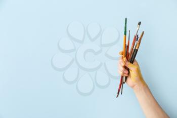 Hand of artist with brushes on color background�