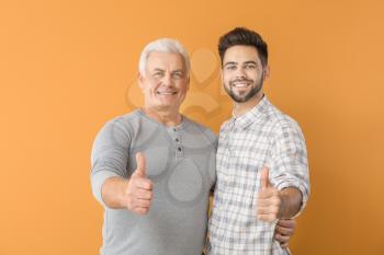 Young man and his father showing thumb-up on color background�