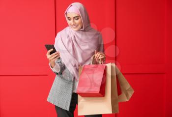 Beautiful Arab woman with shopping bags and mobile phone on color background�