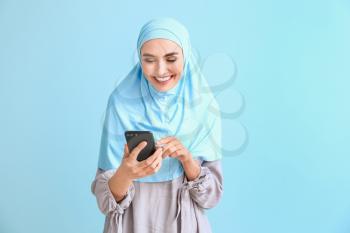 Beautiful Arab woman with mobile phone on color background�
