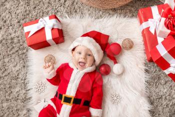Cute little baby in Santa Claus costume and with Christmas gift boxes lying on plaid, top view�