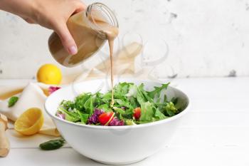 Woman pouring tasty tahini from jar onto vegetable salad in bowl�