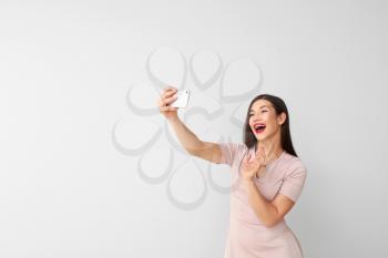 Beautiful young woman taking selfie on light background�