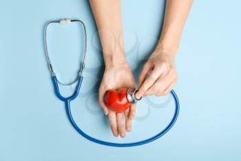 Female hands with red heart and stethoscope on color background. Cardiology concept�