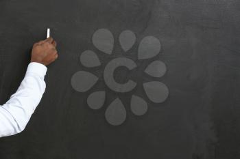 Hand of African-American teacher writing on blackboard in classroom�
