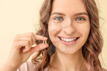 Young woman with fish oil on color background�