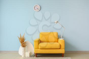 Soft armchair with vase, lamp and candles near color wall in room�