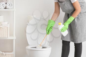 Young woman cleaning toilet in bathroom�