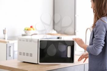 Woman opening modern microwave oven in kitchen�