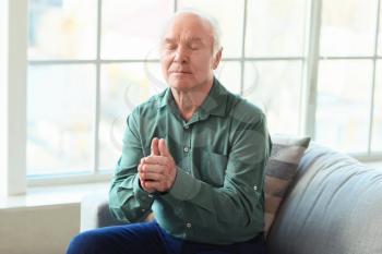 Portrait of praying elderly man at home�