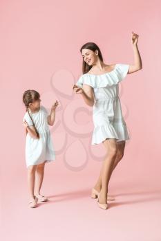 Happy mother and her little daughter dancing against color background�