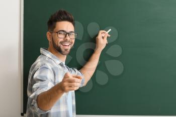 Male teacher writing on blackboard in classroom�