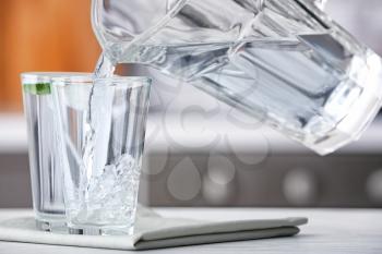 Pouring of fresh water into glass on table in kitchen�