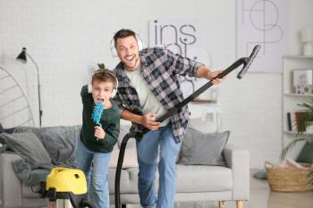 Little boy and his father having fun while hoovering floor in room�