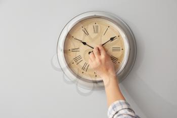 Young man touching arrows of clock on light wall�