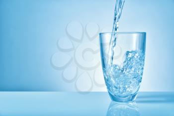 Pouring of fresh water into glass on color background�