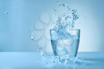 Glass of fresh water with splash on color background�