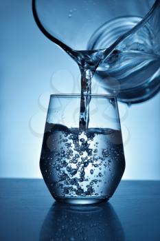 Pouring of fresh water in glass on color background�