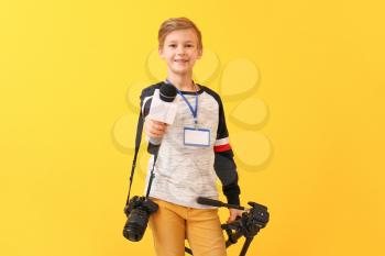 Little journalist with microphone and camera on color background�