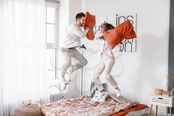 Happy young couple fighting on pillows in bedroom�