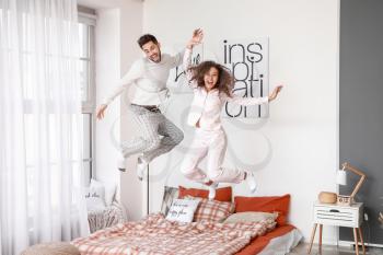 Happy young couple jumping on bed at home�