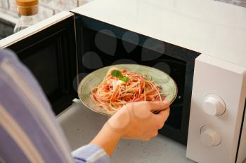 Woman putting plate with food in microwave oven�