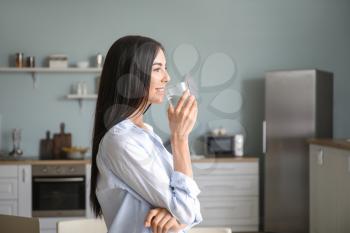 Beautiful young woman drinking water in kitchen�