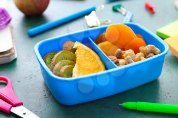 School lunch box with tasty food and stationery on table�