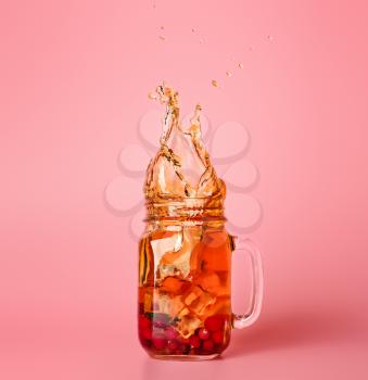 Mason jar of cold tea with splashes on color background�
