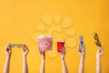 Many hands with popcorn, drink, remote control and eyeglasses on color background�
