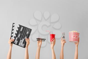 Many hands with popcorn, drink, remote control, movie clapper and eyeglasses on grey background�
