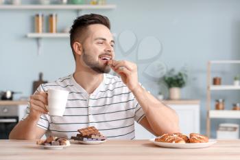 Handsome young man eating chocolate in kitchen�