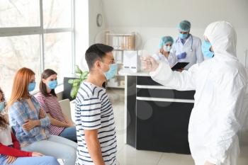 Doctor in protective uniform measuring temperature of male patient in clinic�