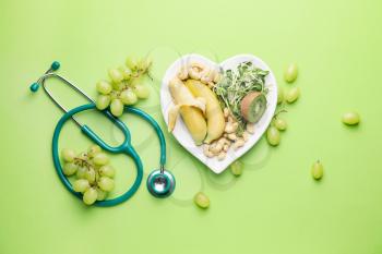 Plate with healthy products and stethoscope on color background�