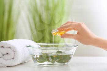 Woman pouring essential oil from bottle into bowl at home�