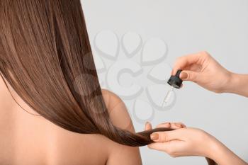 Applying of cosmetics on woman's hair against grey background�