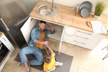 Little son helping his father to repair sink in kitchen�